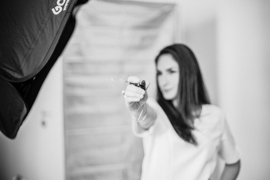 Donna in divisa bianca tende un piccolo strumento verso l'obiettivo accanto al softbox nel backstage in bianco e nero 2020