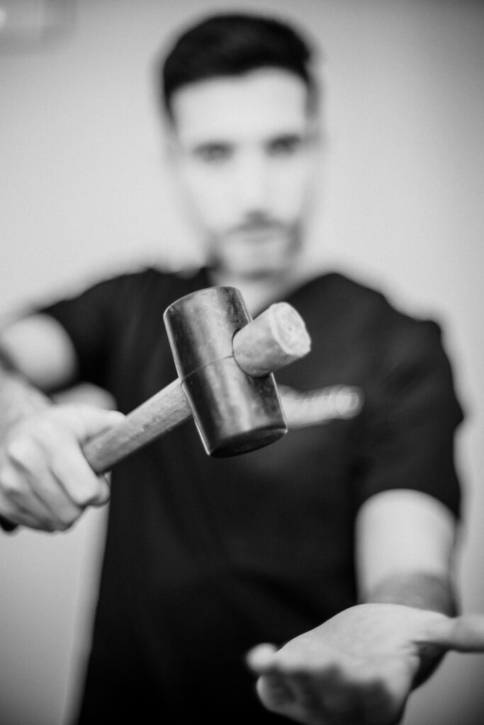 Operatore in divisa nera mostra un martelletto di legno all'obiettivo nel backstage fotografico 2020 di Alta Clinic