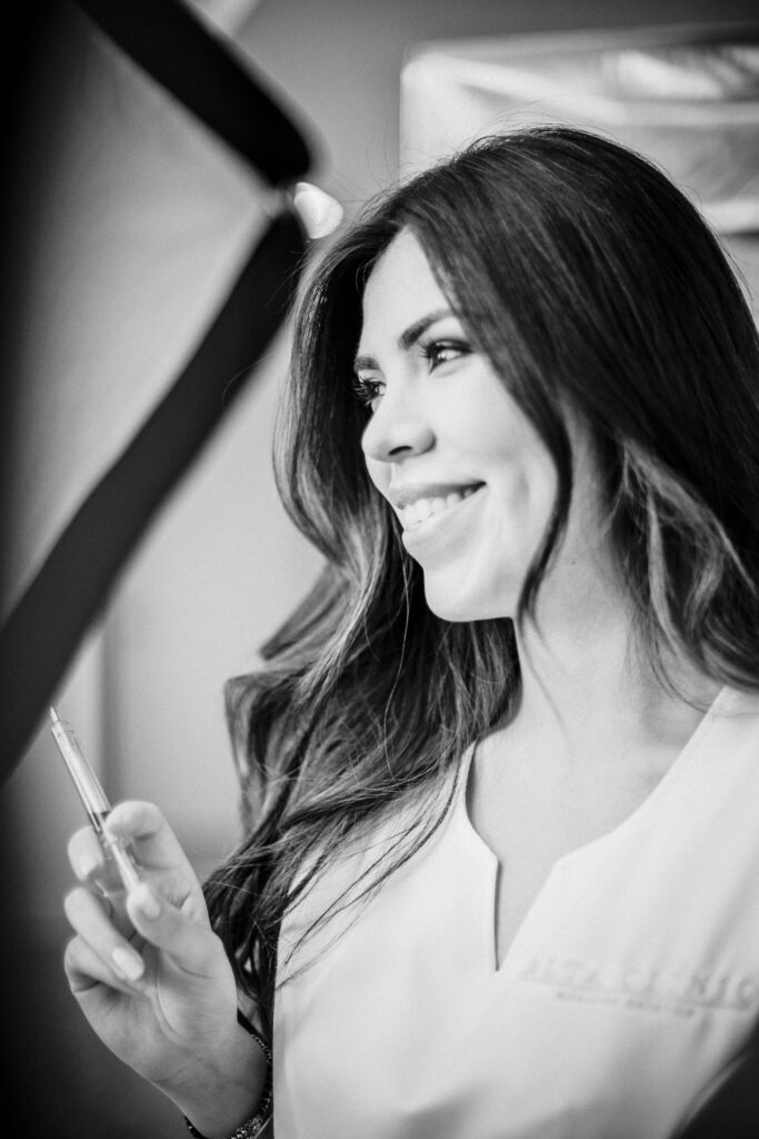 Donna sorridente di profilo con lunghi capelli scuri e divisa bianca nel backstage in bianco e nero di Alta Clinic