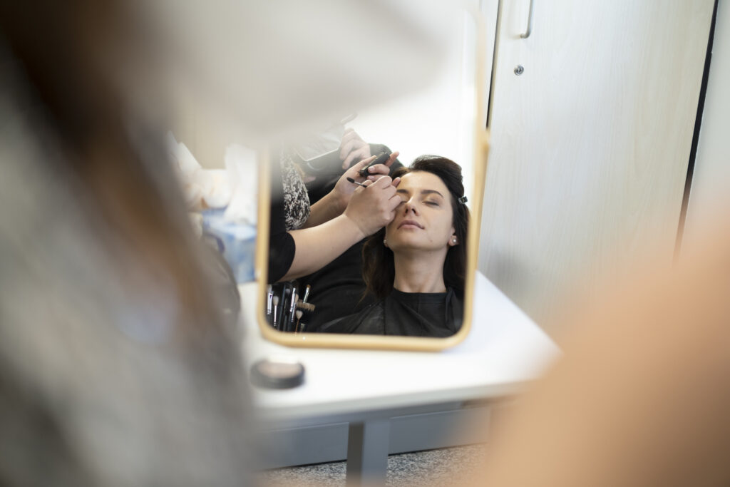 Truccatrice al lavoro riflessa nello specchio durante il backstage del servizio fotografico 2022 di Alta Clinic Bergamo