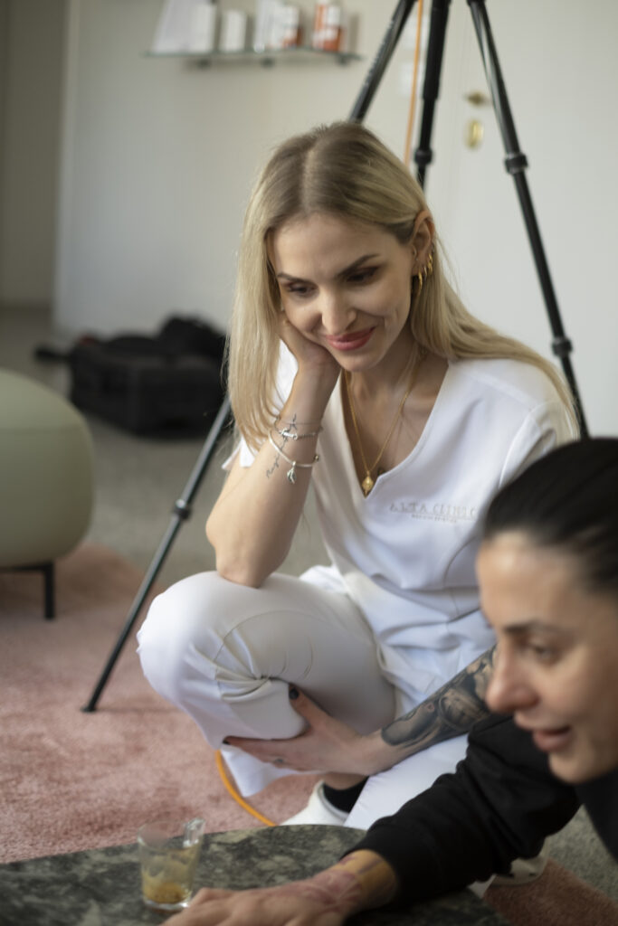 Donna bionda seduta a terra sorride guardando le foto sul portatile nel backstage 2022 di Alta Clinic Bergamo