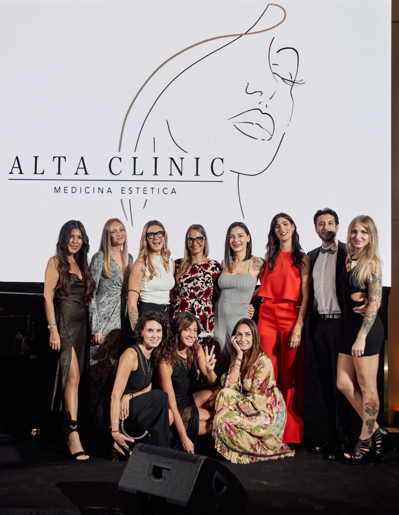 Gruppo di donne e uomini in posa sul palco della Cesvi Charity Night 2023 sotto il logo Alta Clinic medicina estetica