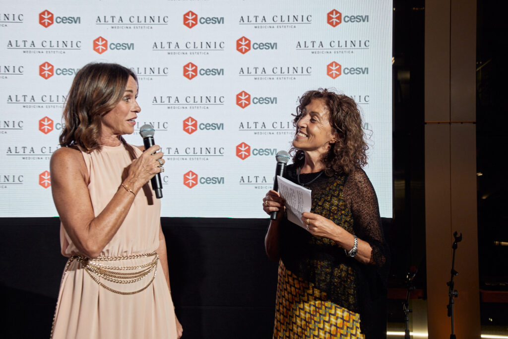 Due donne parlano al microfono davanti al pannello con i loghi Cesvi e Alta Clinic alla Cesvi Charity Night 2023
