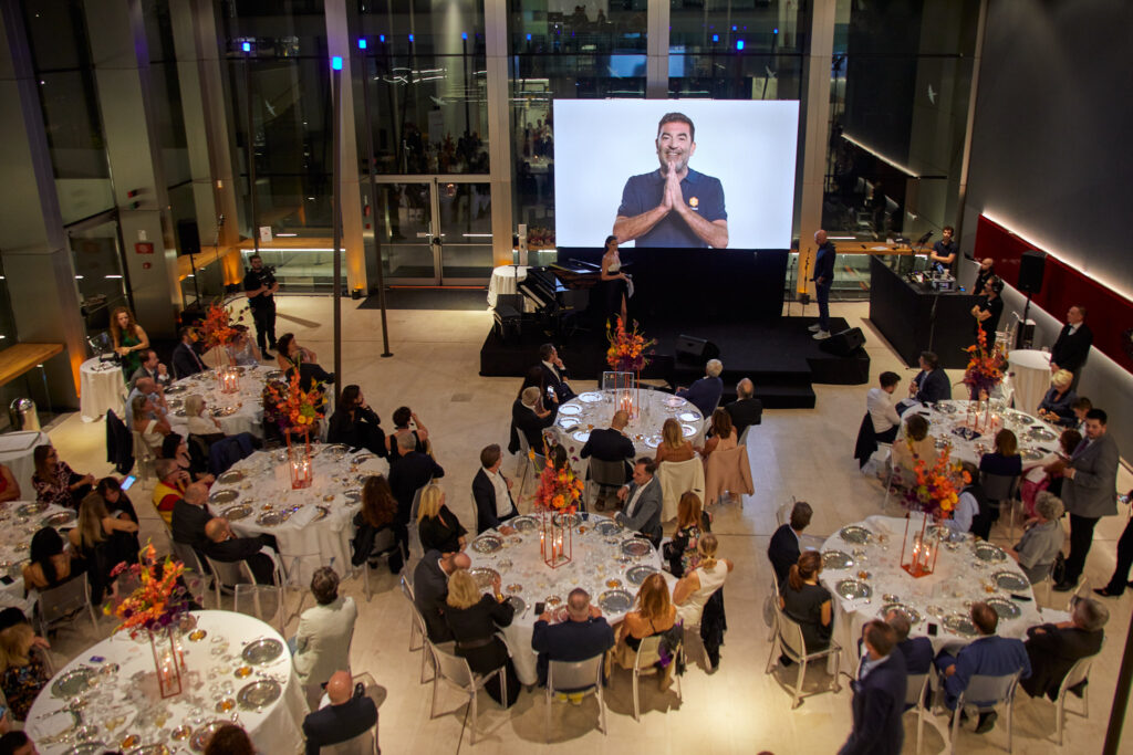 Vista dall'alto della sala con tavoli rotondi e maxischermo durante la cena di beneficenza Cesvi Charity Night 2023