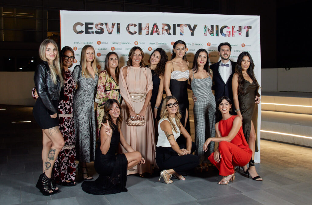 Gruppo di invitate e invitati in abito elegante davanti al pannello della Cesvi Charity Night 2023 con Alta Clinic