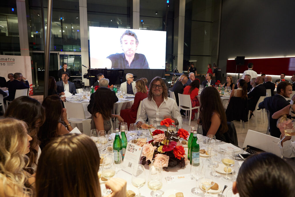 Ospiti ai tavoli della Cesvi Charity Night 2022 mentre sul maxischermo scorre un videomessaggio, serata con Alta Clinic