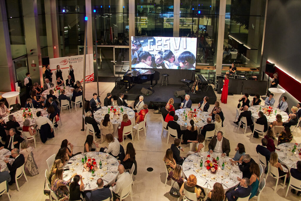 Vista dall'alto della sala con tavoli rotondi e il logo Cesvi sul maxischermo alla Cesvi Charity Night 2022
