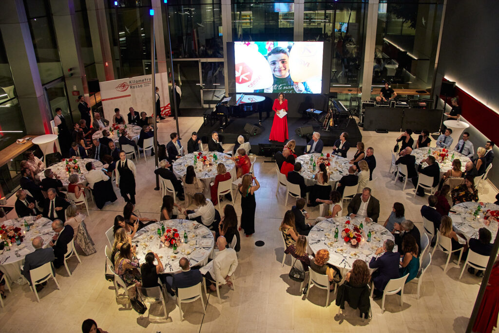 Ospite in abito rosso sul palco davanti al maxischermo, vista dall'alto della cena Cesvi Charity Night 2022
