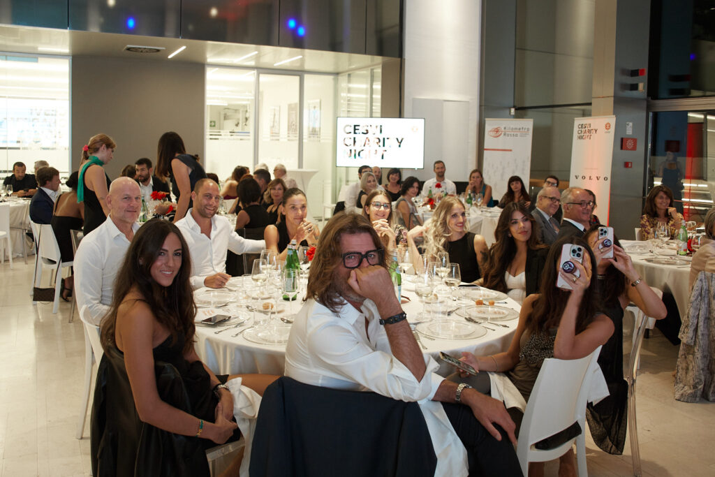 Ospiti al tavolo che sorridono e scattano foto con lo smartphone durante la Cesvi Charity Night 2022