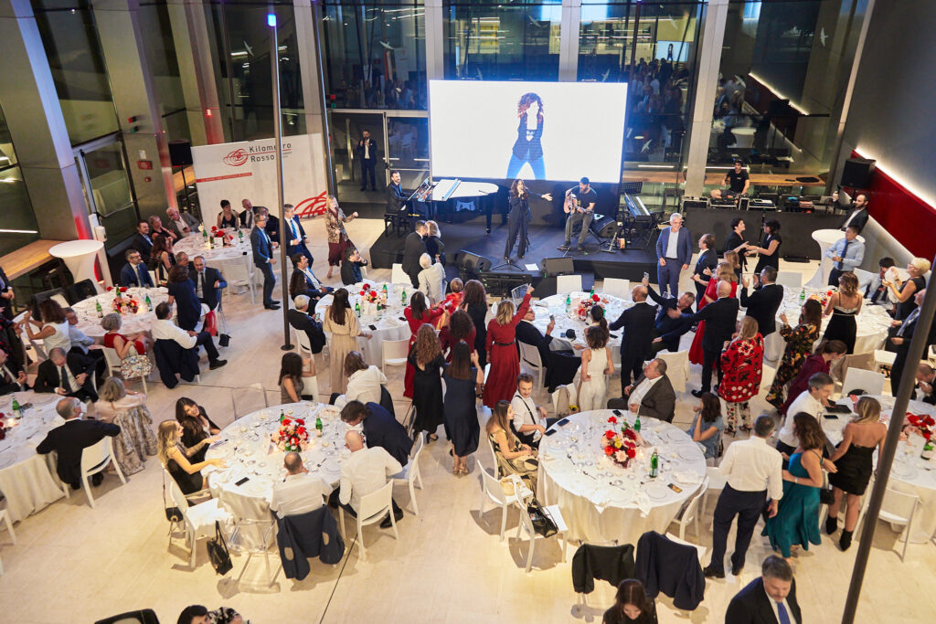 Ospiti in piedi tra i tavoli e maxischermo acceso nella sala della serata benefica Cesvi Charity Night 2022